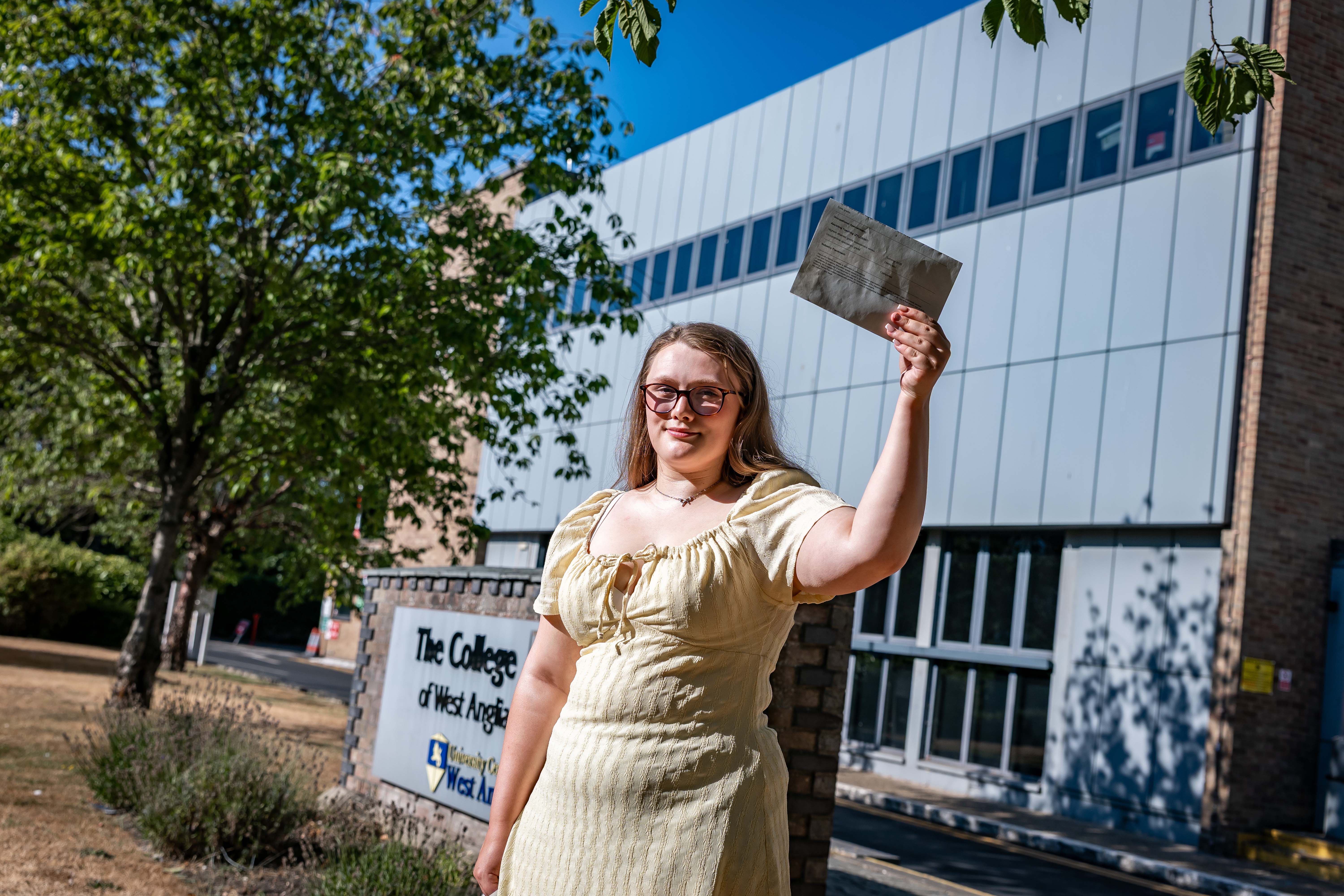 Female student in yellow dress holding up her results