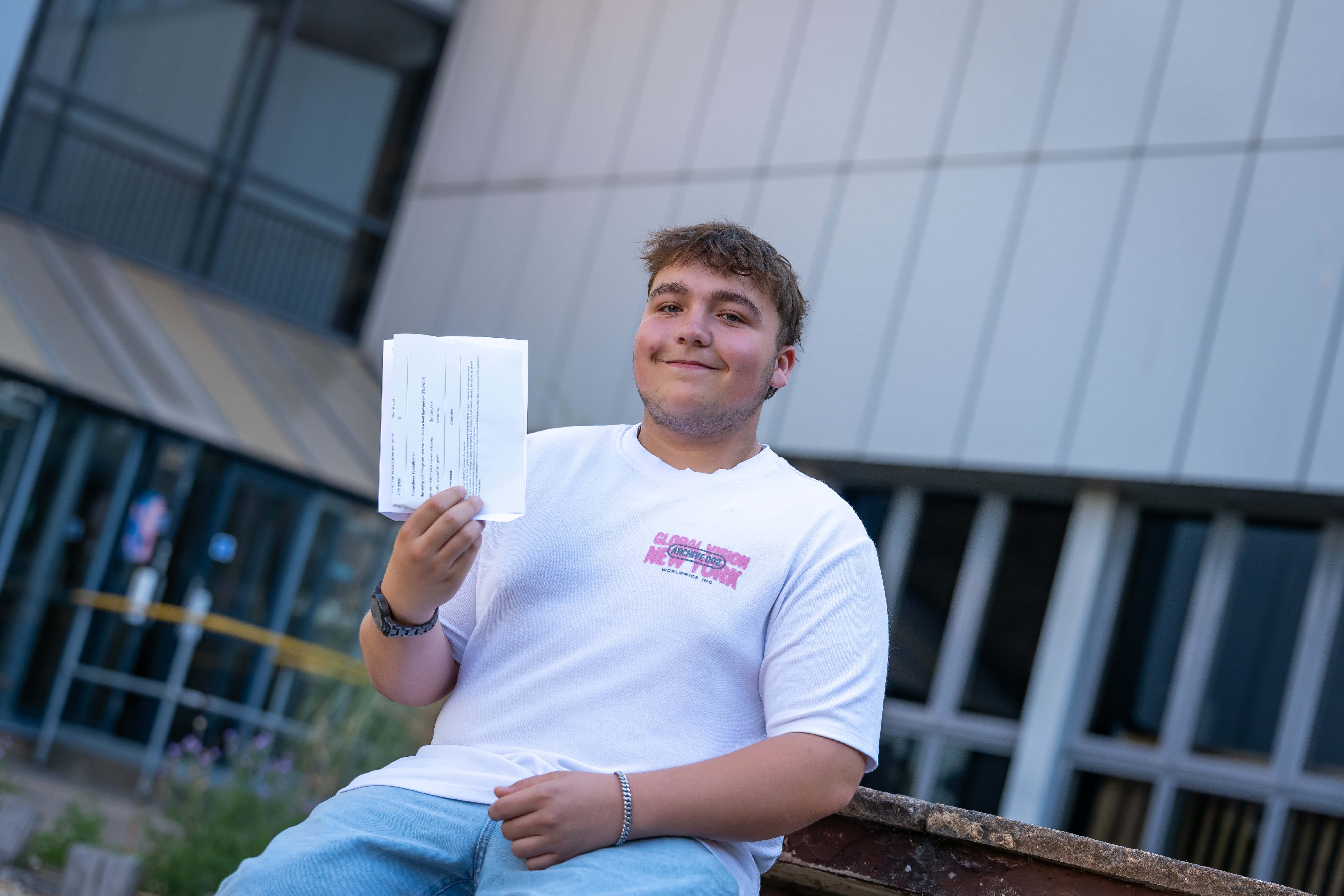 Male student in white tshirt smiling whilst holding results