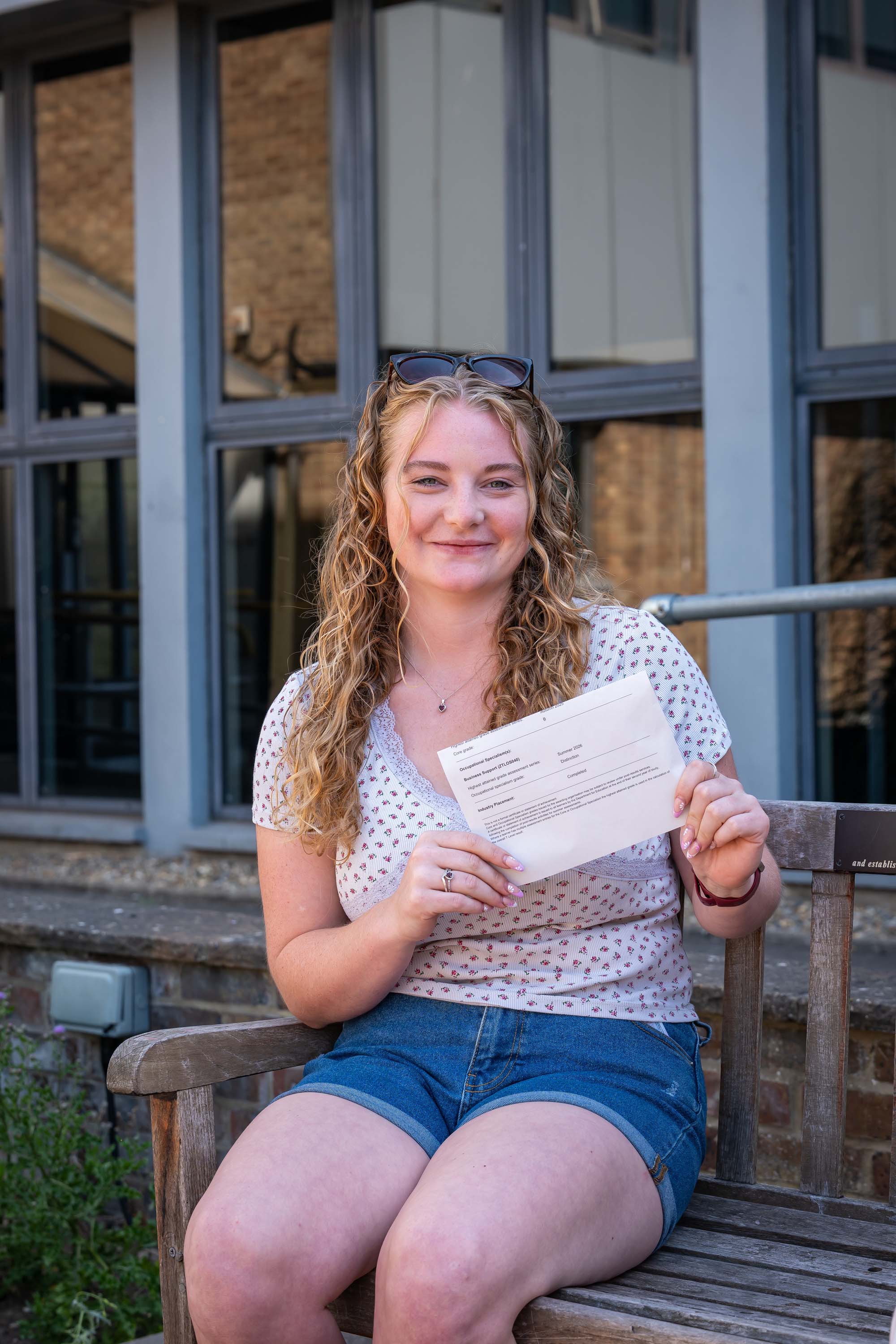 Student on bench smiling holding her results